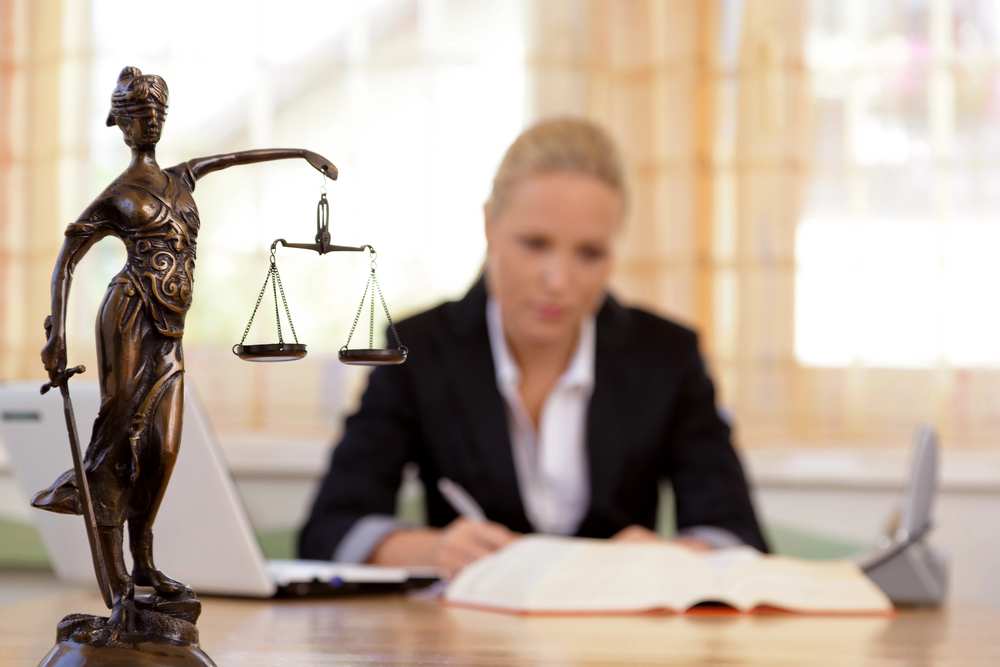 Lawyer at her desk writing a legal document with statue of lady justice nearby at a Lakewood Law Firm